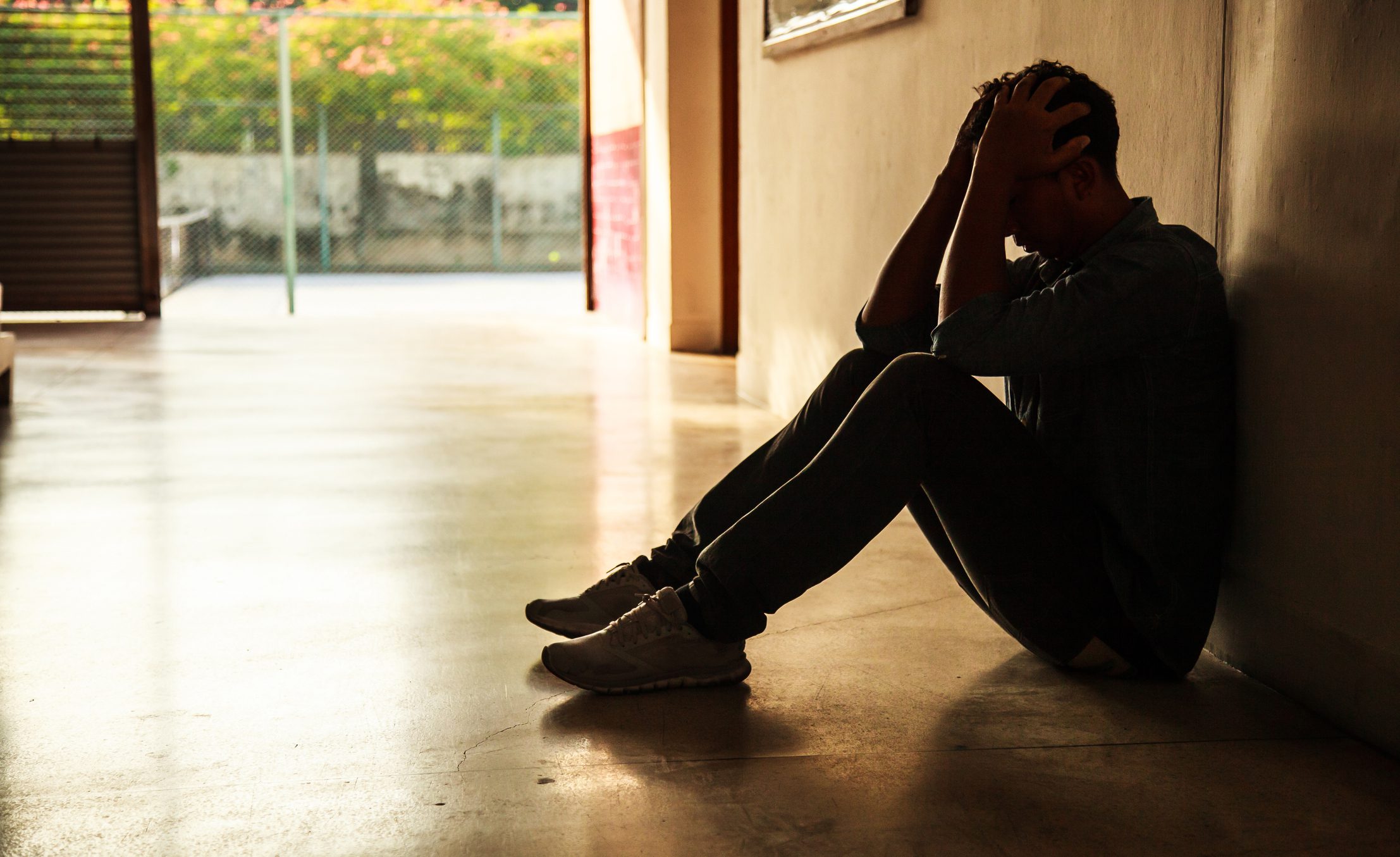 Man sits in a dark hallway covering his face.
